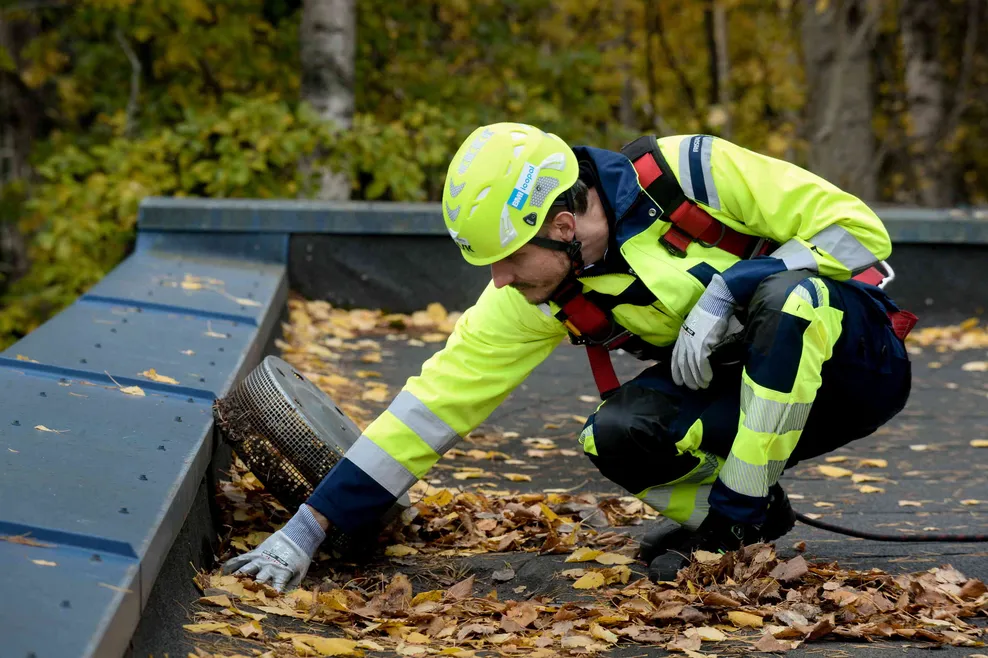Icopal Katto Oyn Kattohuollon työntekijä katolla puhdistamassa kattokaivoa